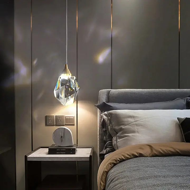 Luminária Pendente LED Cristal Lapidado Gold Larevy, acesa ao lado de uma cama, em quarto moderno com parede cinza