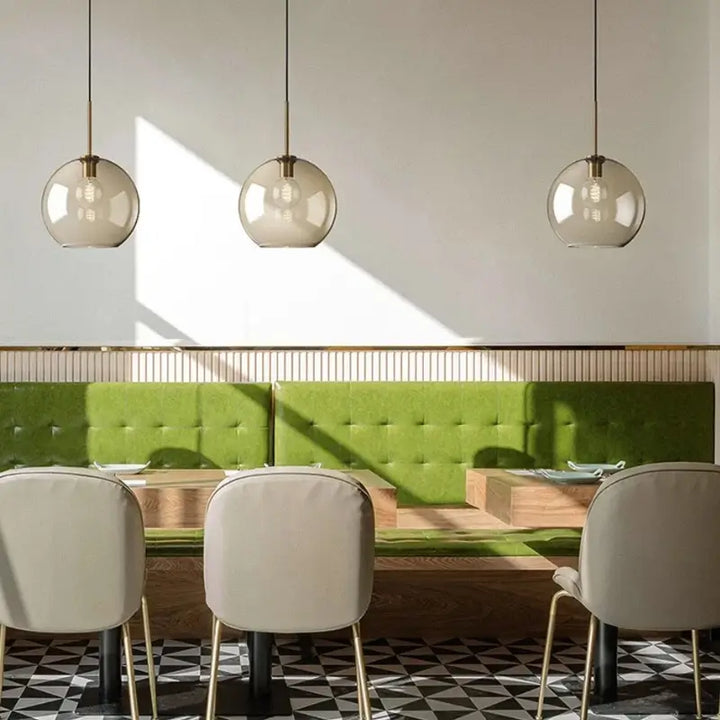 Luminária Pendente Vidro Ambaris Magna trio em restaurante com banco estofado verde e parede bege