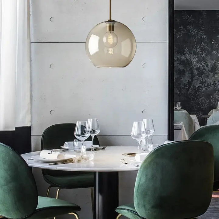 Luminária Pendente Vidro Ambaris Magna sobre mesa de jantar com cadeiras verdes de veludo