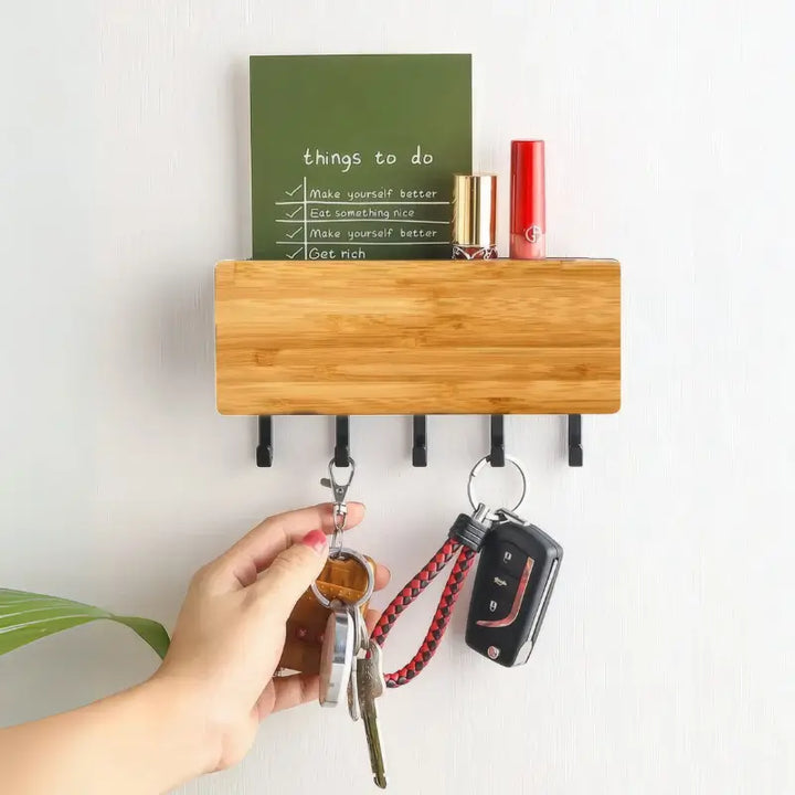 Porta Chaves de Parede em Bambu Orto Preto em uso, com mão pegando chaves, bloco de notas verde e cosméticos